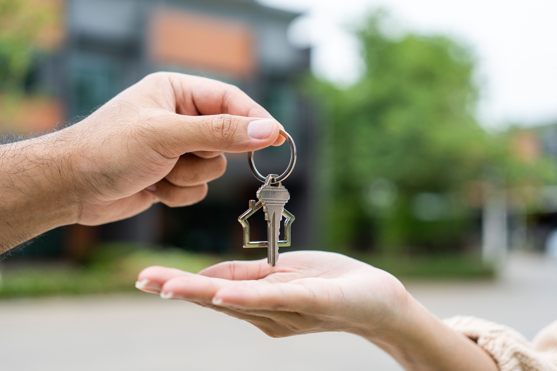 Mujer que compra o alquila una casa nueva que sostiene la llave frente de la nueva casa. Sorprende a una joven asiática feliz que da la llave de la casa y sonríe para alquilar o comprar un apartamento. Concepto de mudanza de reubicación.