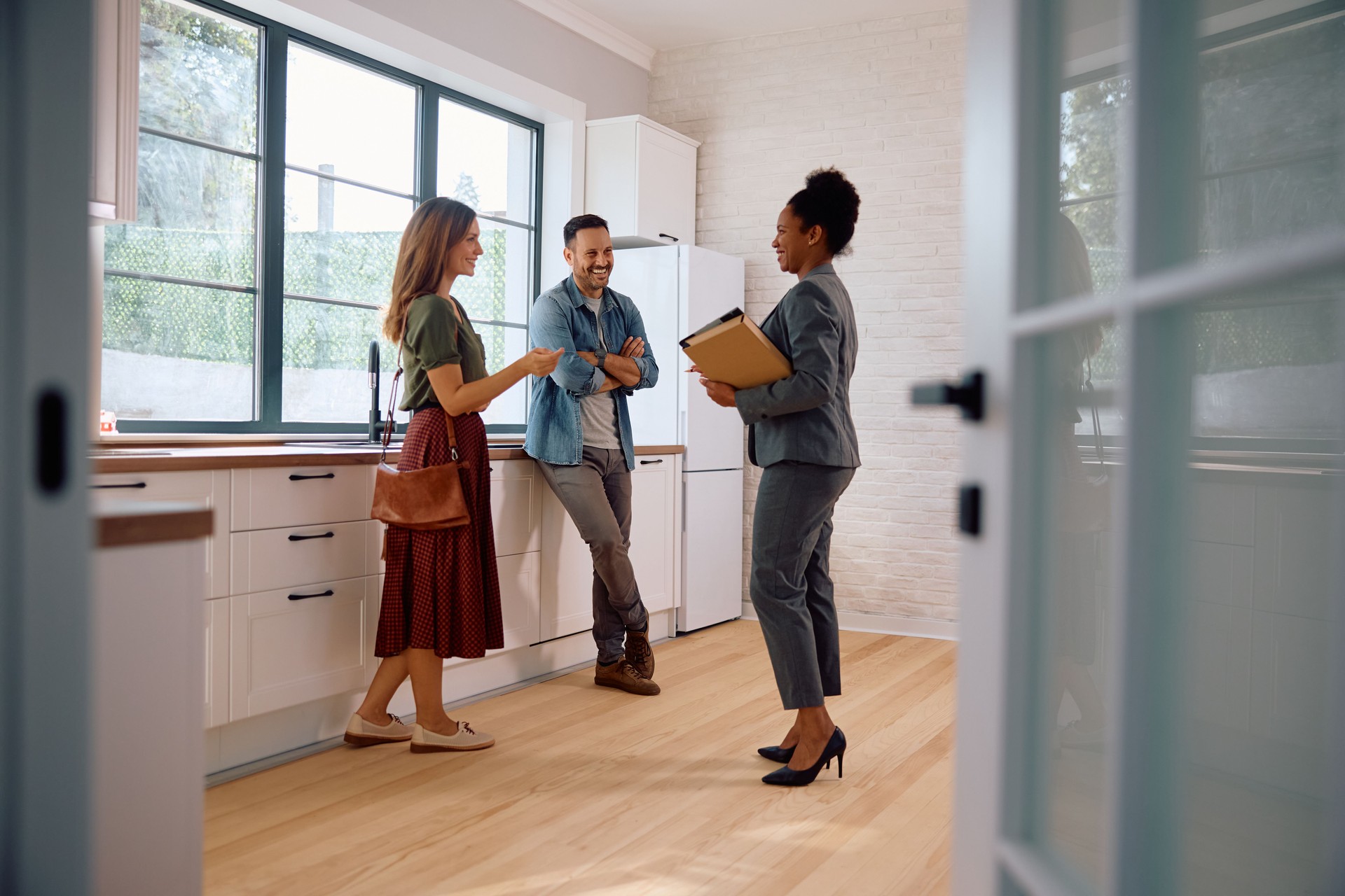 Feliz agente inmobiliario negro y una pareja en la cocina de una casa nueva.